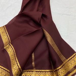 May include: A maroon saree with a gold border. The border features a repeating pattern of stylized floral motifs.