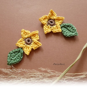 Könnte beinhalten: Zwei gehäkelte Sonnenblumen-Applikationen mit grünen Blättern. Die Sonnenblumen sind gelb mit braunen Zentren. Die Blätter sind dunkelgrün.