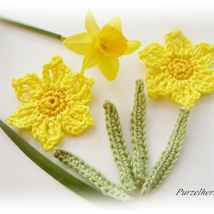 Könnte beinhalten: Gehäkelte Narzissenblüten mit grünen Stielen. Die Blüten sind gelb und haben ein detailliertes Häkeldesign. Die Stiele sind hellgrün.
