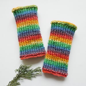 Könnte beinhalten: Ein Paar gestrickte Armstulpen in Regenbogenfarben. Die Farben umfassen Rot, Orange, Gelb, Grün, Blau und Violett. Die Bündchen sind dunkler und die Armstulpen sind etwa 20 cm lang.