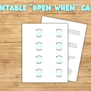 Peut inclure: Cartes "Open When" imprimables sur une surface en bois. Les cartes présentent un motif de cœur turquoise avec les mots "When you feel unmotivated". Le texte "Printable Open When Cards" est en haut en lettres turquoise.