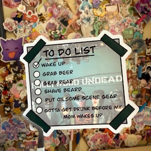 May include: A white sticker with the text "TO DO LIST" and a list of tasks, including "WAKE UP" and "GRAB BEER." The sticker is attached to a corkboard covered in colorful stickers of various characters.