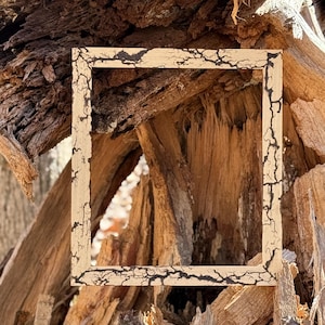 May include: A rectangular wooden picture frame featuring a light beige finish with dark, intricate, branching fractal patterns burned into the surface. The frame has a clean, flat profile and a hollow center, showcasing a natural, high-contrast design.