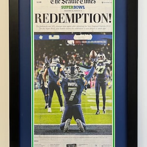 May include: Framed Seattle Times newspaper front page with the headline "REDEMPTION!" and a photo of a football player kneeling on the field. The newspaper is from February 9, 2015, and commemorates the Super Bowl.