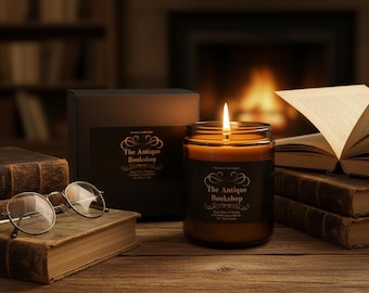 May include: A lit candle in a glass jar with a black label reading The Antique Bookshop, placed next to a black box with a matching label, a pair of round metal-rimmed glasses, and several old books with worn covers on a wooden surface.