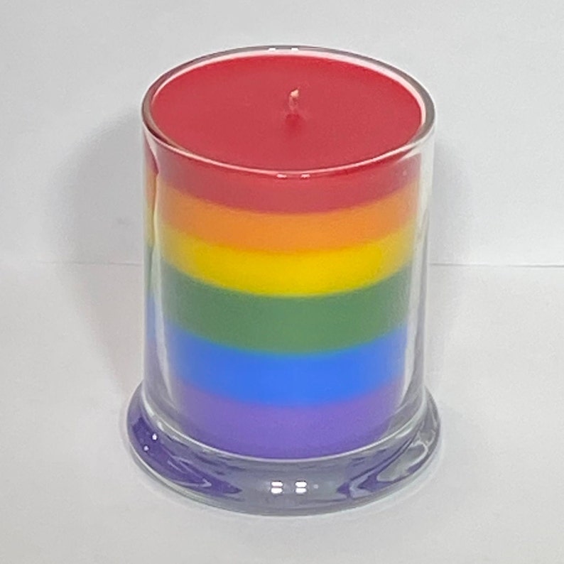 Op de afbeelding: Een regenboog-gekleurde gelaagde kaars in een glazen pot met een rode bovenste laag, oranje, geel, groen, blauw en paarse lagen.