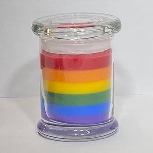 Op de afbeelding: Een regenboogkleurige gelaagde kaars in een glazen pot met deksel. De kaars is gelaagd met rode, oranje, gele, groene, blauwe en paarse was.