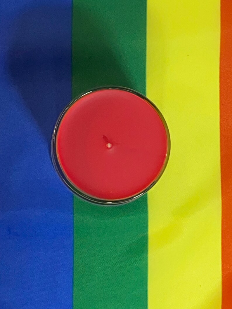 Op de afbeelding: Een rode kaars in een glazen pot, op een regenboogkleurige stoffen achtergrond.