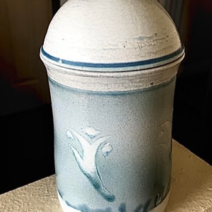May include: A white ceramic jar with a blue and white floral design. The jar has a lid and is decorated with a blue band around the top.
