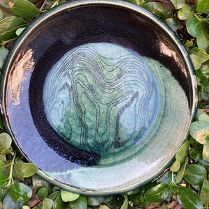 May include: A ceramic plate with a dark blue and green glaze. The plate has a swirling pattern in the glaze.