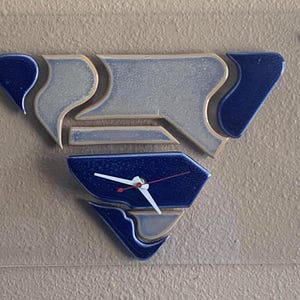 May include: A blue and brown ceramic clock with a white face and hands. The clock is shaped like a triangle and has a unique design.