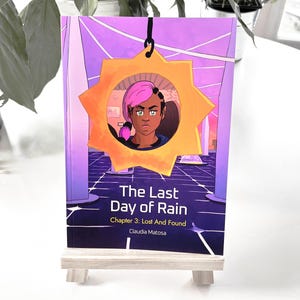 Puede incluir: Una portada de libro con un esquema de color morado, rosa y amarillo. La portada presenta un personaje de dibujos animados con cabello rosado y ojos verdes. El título del libro es "The Last Day of Rain" y el subtítulo es "Chapter 3: Lost And Found". El autor es Claudia Matosa.