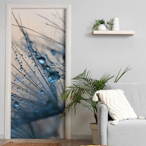 Könnte beinhalten: Eine rechteckige Tür mit einem großformatigen Fotodruck eines Löwenzahnsamenkopfes, der mit bläulich getönten Wassertropfen bedeckt ist. Das Bild zeigt feine, strahlenförmige Filamente und kugelförmige Tautropfen vor einem hellen Hintergrund.