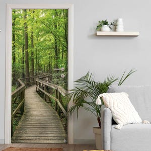 Könnte beinhalten: Ein Türtapeten-Wandbild mit einer realistischen Waldszene, bei der ein hölzerner Bohlenweg durch üppig grüne Bäume führt. Die Perspektive erzeugt einen immersiven Blick auf einen Naturpfad mit detaillierten Holzgeländern und Laub.