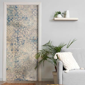 Könnte beinhalten: Eine Tür, die mit einer dekorativen Klebefolie mit einem sich wiederholenden Muster aus blauen und weißen Fliesen bedeckt ist. Das Design umfasst verschiedene geometrische Formen, komplexe Wirbel und klassische Mäandermuster in Vintage-Optik.