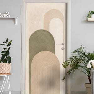 Könnte beinhalten: Eine Tür mit einem grafischen Design aus überlappenden Bögen in Salbeigrün, Beige und Creme. Die Oberfläche wirkt strukturiert und zeigt feine, konzentrische Linien im unteren Bogen. Ein silberner Metalltürgriff ist an der Tür angebracht.