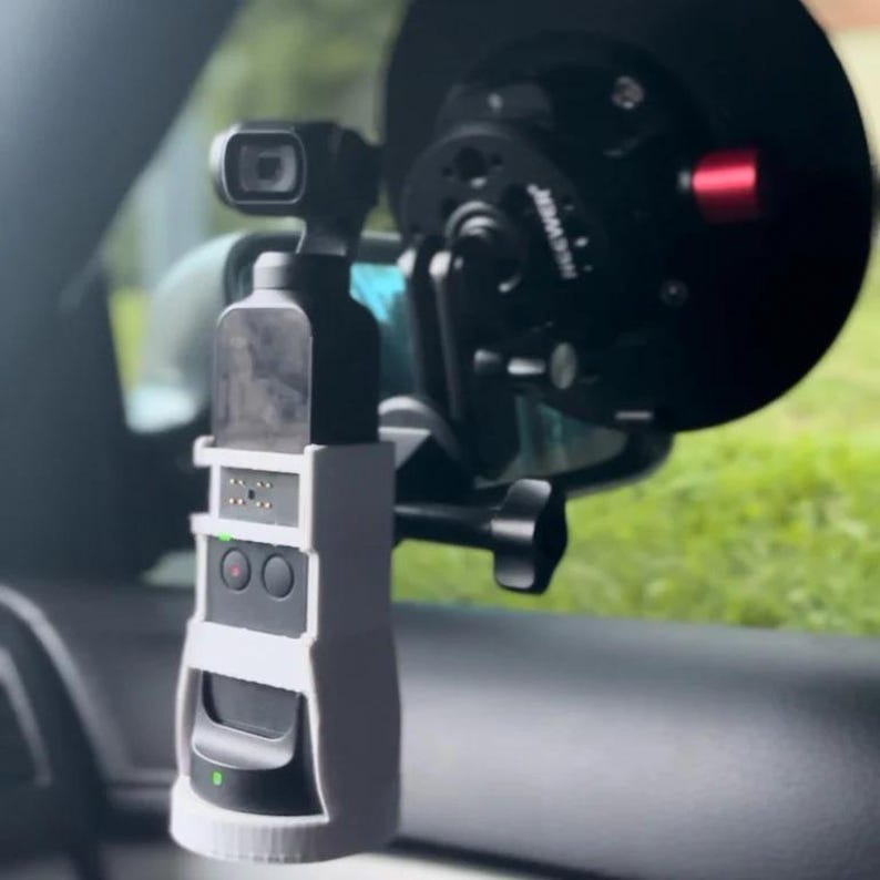 Puede incluir: Un soporte de impresi&oacute;n 3D blanco para una c&aacute;mara GoPro, fijado al espejo retrovisor de un coche. La c&aacute;mara es negra y tiene una peque&ntilde;a pantalla en el lateral.