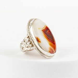 Op de afbeelding: Een zilveren ring met een ovale agaat-steen. De steen is wit met rode en bruine strepen.