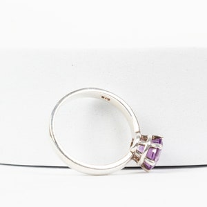 K&ouml;nnte beinhalten: Ein silberner Ring mit einem violetten Edelstein, der in einer Krappenfassung sitzt. Der Ring ist innen mit "925" gekennzeichnet.
