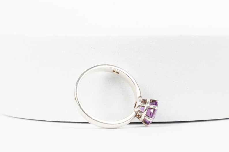K&ouml;nnte beinhalten: Ein silberner Ring mit einem violetten Edelstein, der in einer Krappenfassung sitzt. Der Ring ist innen mit "925" gekennzeichnet.