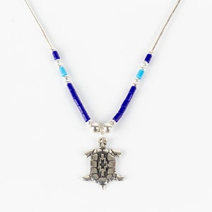 Può includere: Una collana d'argento con perline blu e turchesi e un ciondolo a forma di tartaruga d'argento.