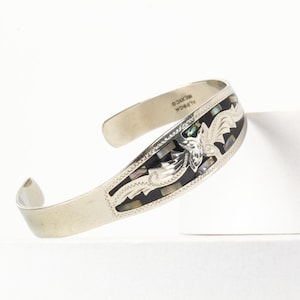 Pode incluir: Pulseira de punho de prata com incrustações decorativas de peças de concha pretas e iridescentes. A pulseira apresenta um design floral e o texto "ALPACA MEXICO".