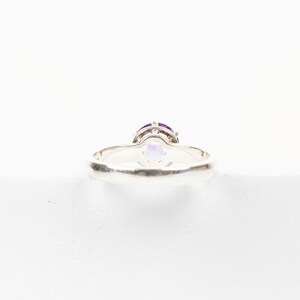 K&ouml;nnte beinhalten: Ein silberner Ring mit einem violetten Edelstein, der in einer Krappenfassung sitzt. Der Ring wird von unten gezeigt, wodurch die Fassung und die Unterseite des Steins sichtbar werden.