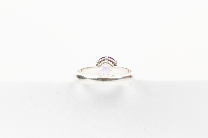 K&ouml;nnte beinhalten: Ein silberner Ring mit einem violetten Edelstein, der in einer Krappenfassung sitzt. Der Ring wird von unten gezeigt, wodurch die Fassung und die Unterseite des Steins sichtbar werden.