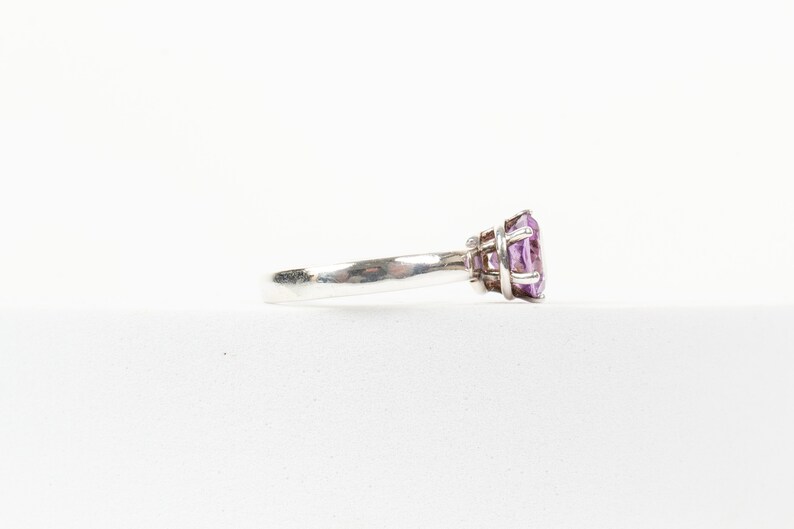 K&ouml;nnte beinhalten: Ein silberner Ring mit einem gro&szlig;en, facettierten, violetten Edelstein, der in einer Krappenfassung sitzt.