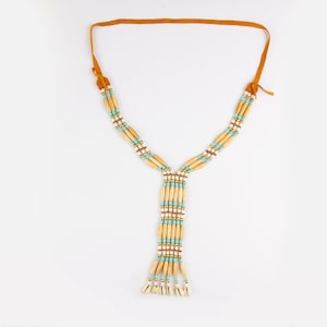 Op de afbeelding: Een bruine leren ketting met een kralenhanger. De kralen zijn bruin, wit en turquoise. De hanger is gemaakt van meerdere kralenstrengen en heeft een franje aan de onderkant.