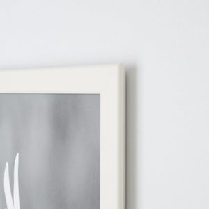 Może przedstawiać: Oprawiona grafika z białą ramą i szarym tłem. Grafika ma białe abstrakcyjne kształty. Rama ma prosty, nowoczesny design, a og&oacute;lna estetyka jest minimalistyczna i czysta.