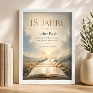 Op de afbeelding: Een wit ingelijste wanddecoratie met een landschapsillustratie van een pad dat naar een zonsopgang leidt, met een open boek op de voorgrond. De tekst luidt: 18 JAHRE, Lieber Paul, 18 Kapitel voller Erinnerungen. Das schönste wartet noch. Alles Liebe, Deine Familie.