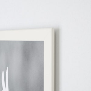 May include: A white picture frame with a gray and white photograph inside. The frame is on a white wall.