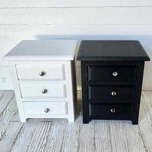 May include: Two wooden nightstands with three drawers each. The nightstand on the left is white and the nightstand on the right is black.