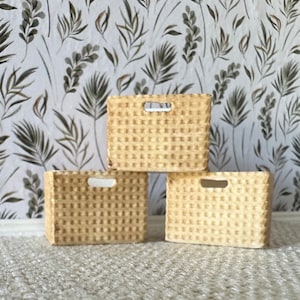May include: Three woven storage baskets with a light brown color and a grid pattern. The baskets are stacked on top of each other.