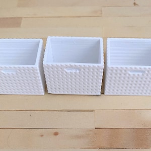 May include: Three white wicker baskets with a woven pattern. The baskets are empty and have a rectangular shape.