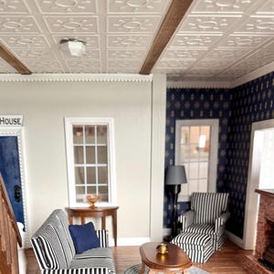 May include: Miniature living room scene with a striped sofa and armchair. The room features a white ceiling with decorative panels, a wooden floor, and a blue accent wall. A small table and a rug complete the scene.