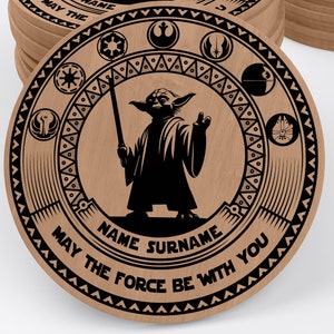 May include: A round wooden coaster with a black and white design featuring Yoda from Star Wars. The coaster has a decorative border with symbols from the Star Wars universe. The text "NAME SURNAME MAY THE FORCE BE WITH YOU" is printed on the coaster.
