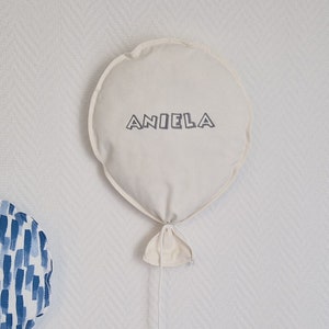 May include: A white fabric balloon with a string attached. The balloon has the name "Aniela" embroidered on it in a gray font.