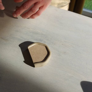 May include: A light brown, rounded, ceramic dish with a slightly raised edge. The dish is sitting on a white surface.