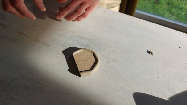 May include: A light brown, rounded, ceramic dish with a slightly raised edge. The dish is sitting on a white surface.