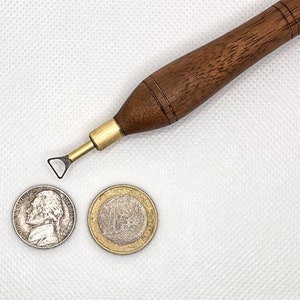 May include: A close-up of a wooden tool with a small metal blade, a silver coin with a portrait of a man, and a gold coin with a design on it.