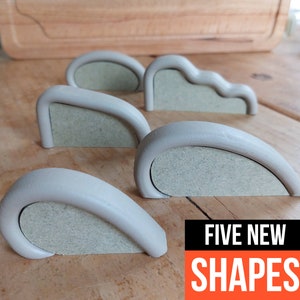 May include: Five different shaped, light gray, smooth, rounded, decorative pieces with a light gray, textured, flat surface on the back. The text "FIVE NEW SHAPES" is printed in orange on a black background.
