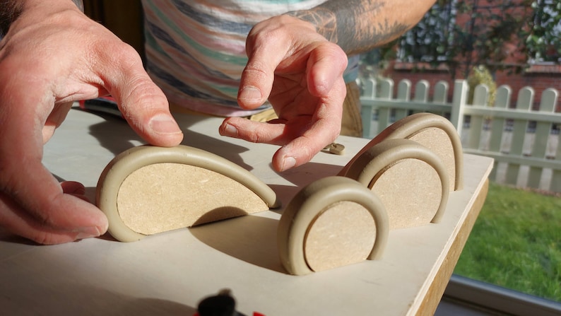 May include: Four beige ceramic arches of varying sizes, arranged in a row on a light wood surface. The arches are made of a smooth, rounded material and have a slightly textured finish.
