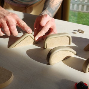 May include: A person is working on a table with several ceramic pieces. The pieces are in various shapes, including arches and triangles. The person is using a tool to shape the clay.
