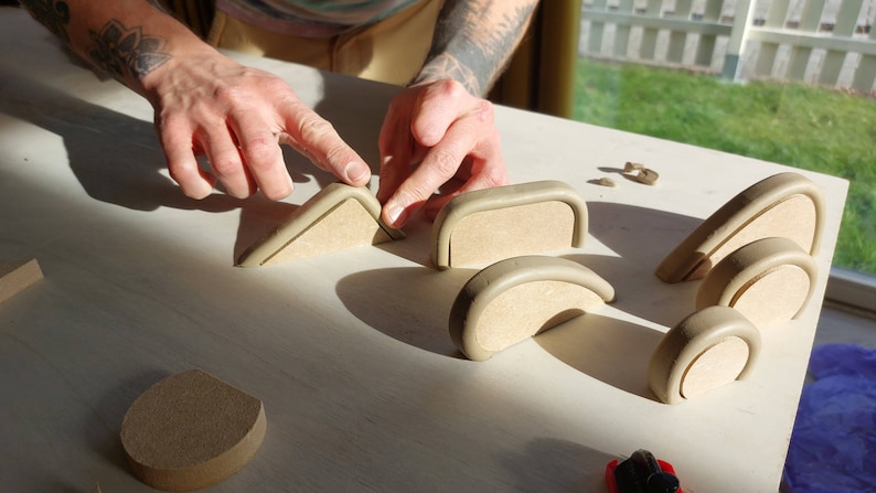May include: A person is working on a table with several ceramic pieces. The pieces are in various shapes, including arches and triangles. The person is using a tool to shape the clay.