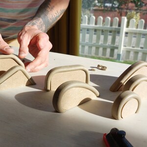 May include: A set of unfinished wooden arches and circles in various sizes, arranged on a light wood surface. The arches are made of a light brown wood and have a smooth, rounded edge. The circles are also made of light brown wood and have a smooth, flat surface. The arches and circles are arranged in a pattern that suggests they are part of a larger project.