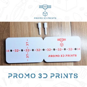 Può includere: Parti bianche stampate in 3D con la scritta "PROMO 3D PRINTS". Le parti includono uno strumento di misurazione con numeri e un logo, insieme a due piccoli pezzi cilindrici bianchi. Lo strumento di misurazione ha i numeri 16, 32 e 37.