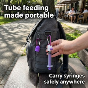 Pu&ograve; includere: Uno zaino grigio con dettagli viola e argento, progettato per il trasporto di forniture mediche. L'immagine mostra una siringa viola e un tappo viola attaccati allo zaino con moschettoni. Il testo sull'immagine recita "Tube feeding made portable" e "Carry syringes safely anywhere."