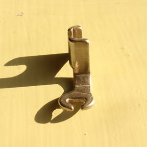 Pode incluir: Um pé de máquina de costura dourado com um design curvo de extremidade aberta. O pé é projetado para uso com uma máquina de costura.